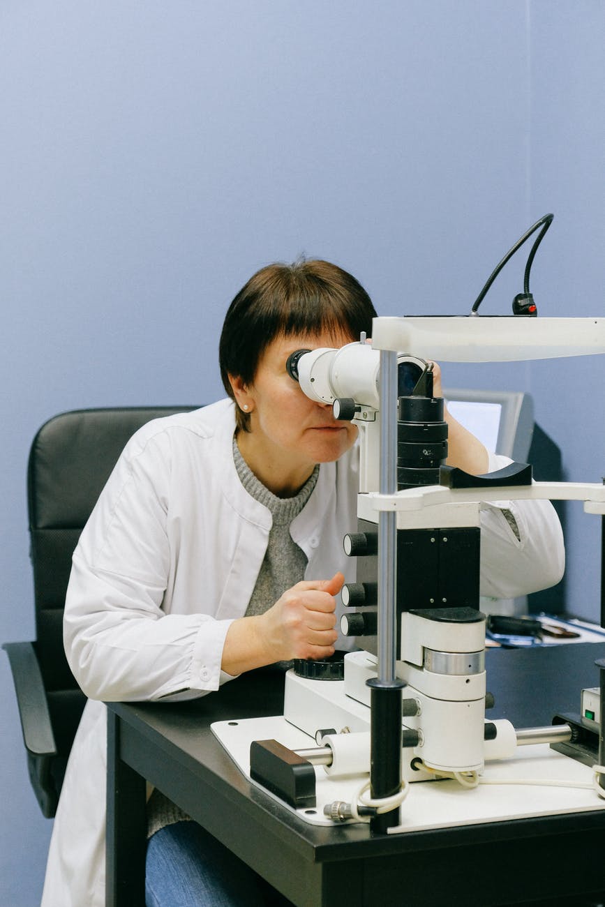 anonymous female scientist looking through slit lamp microscope